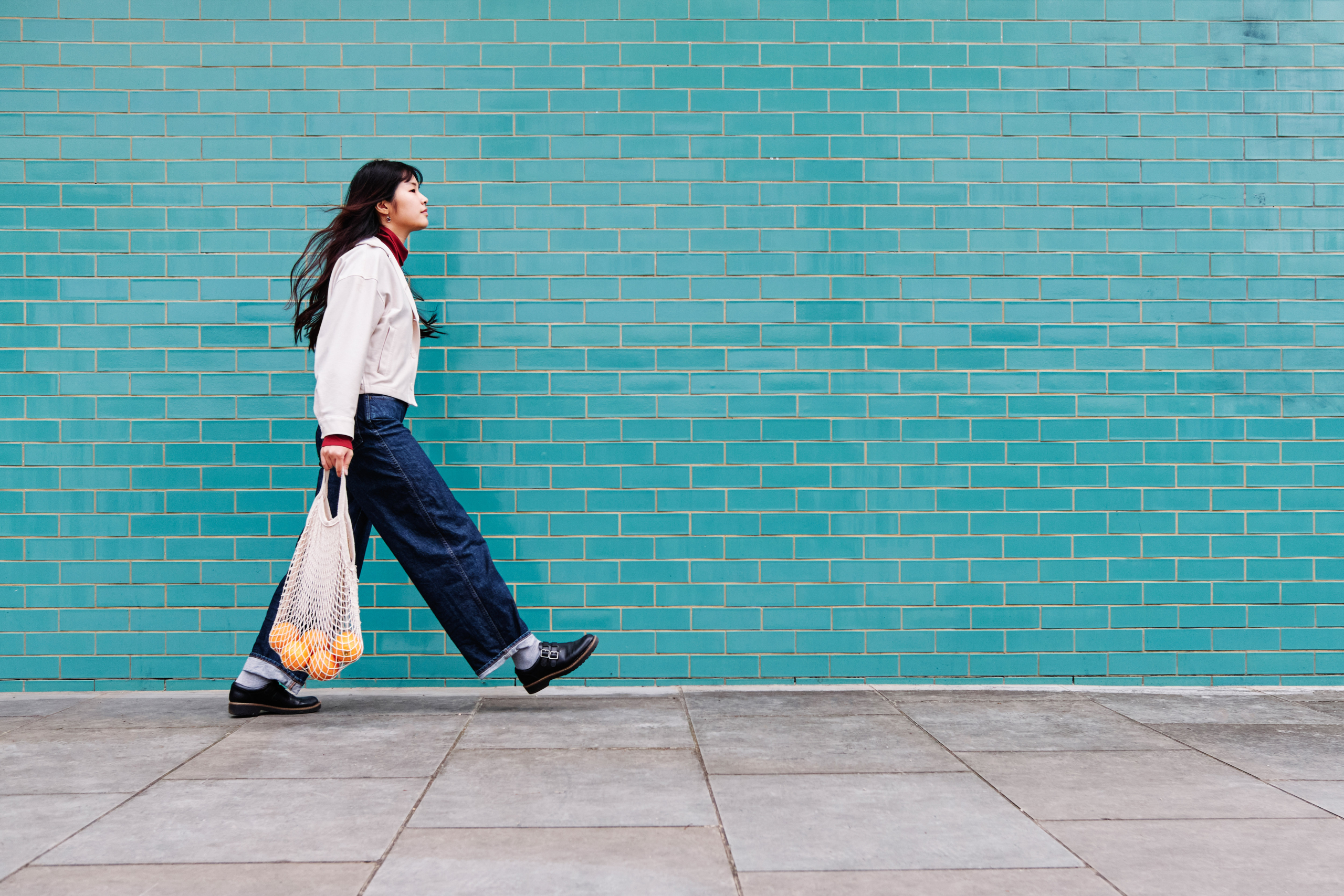 Person walking down the street with a bag of oranges